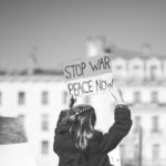 a woman holding a sign that says stop war peace now